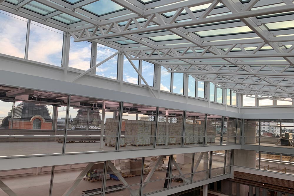 Tak med takfönster som släpper in ljus, synliga metallbjälkar och fönster mot intilliggande lokaler.